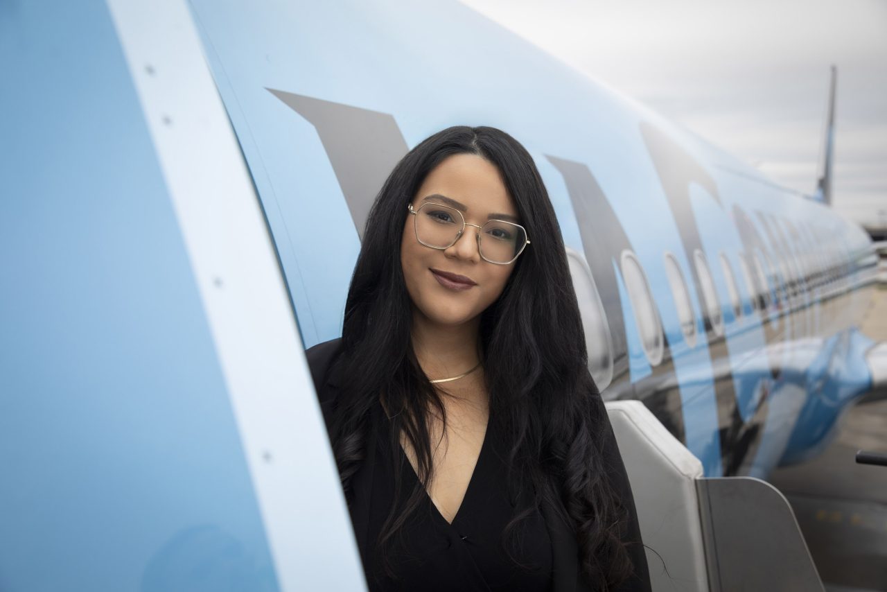 Photo de portrait d'une femme qui regarde dans l'objectif à côté de la porte avant d'un airbus, on voit le fuselage derrière elle