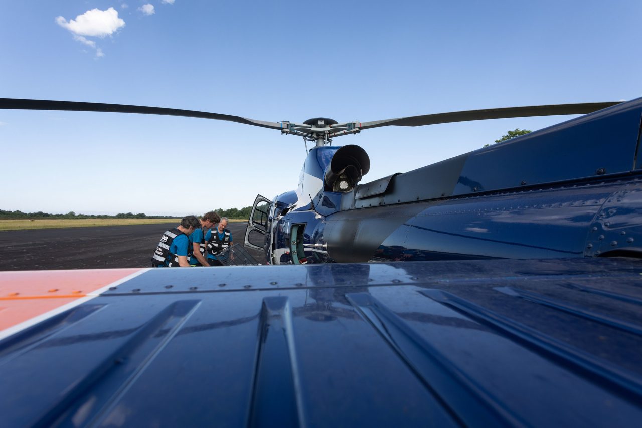 Sur un aérodrome, une équipe de 3 collaborateurs de l'ASNR installent des airbornes sur un hélicoptère Écureuil de couleur bleu afin de pratiquer des mesures héliportés