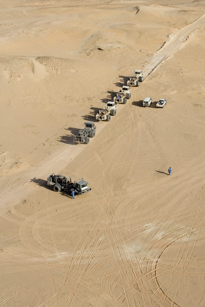 Photographie industrielle aérienne par drone de 5 camions vibrateurs dans le désert effectuant une campagne d'acquisition sismique.