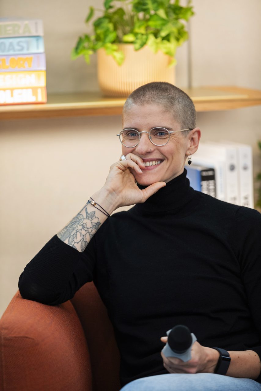 Portrait de Marie Patouillet coureuse cycliste médaillé d'or aux JOP de Paris 2024, elle est souriante, assise dans un fauteuil et tient un micro à la main lors d'un événement organisé par Moët-Hennessy.